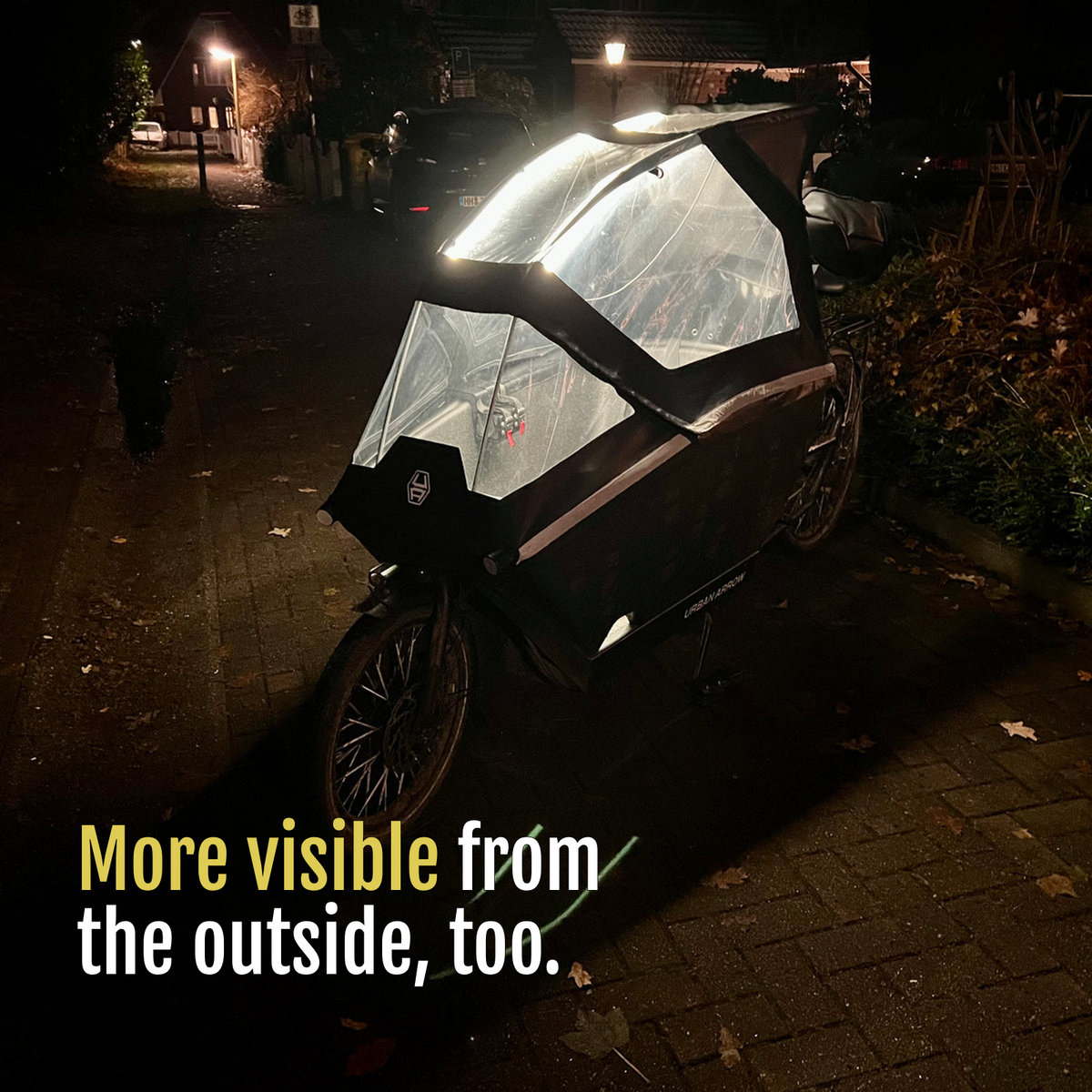 [en] Exterior view of a cargo bike with its canopy illuminated by CargoGLOW at night. More visible from the outside, too.