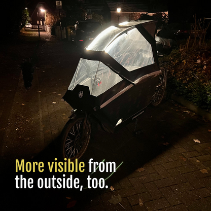 [en] Exterior view of a cargo bike with its canopy illuminated by CargoGLOW at night. More visible from the outside, too.