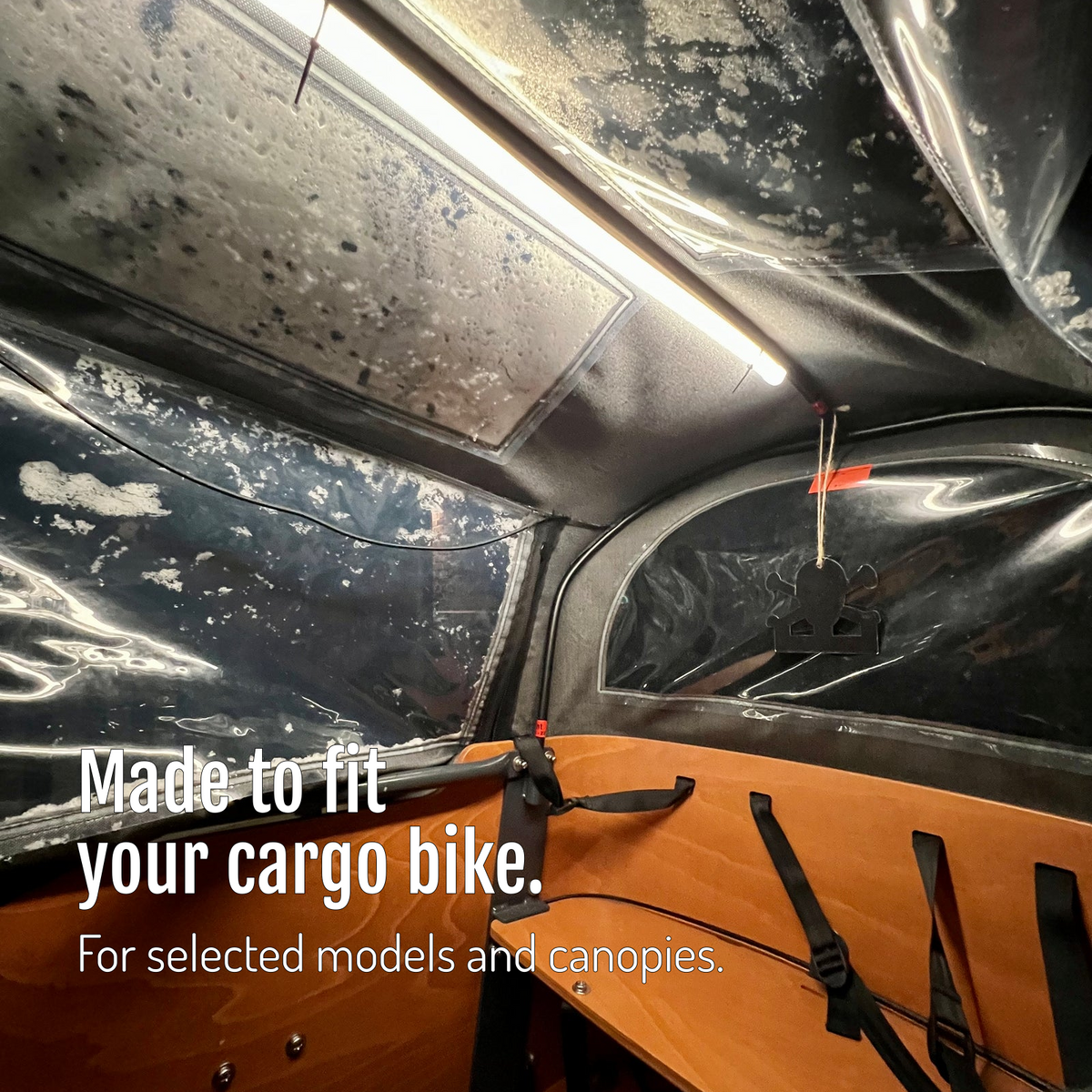 [en] CargoGLOW beneath the canopy of a cargo bike box with an orange interior and seat. Versions made to fit selected models and canopies.