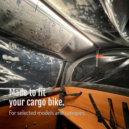 [en] CargoGLOW beneath the canopy of a cargo bike box with an orange interior and seat. Versions made to fit selected models and canopies.